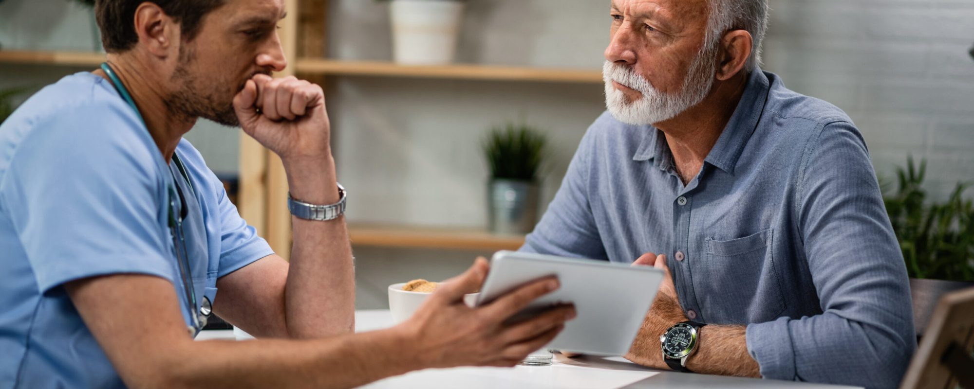 Serious mature man having consultations with his doctor who is showing him medical test analysis on digital tablet.