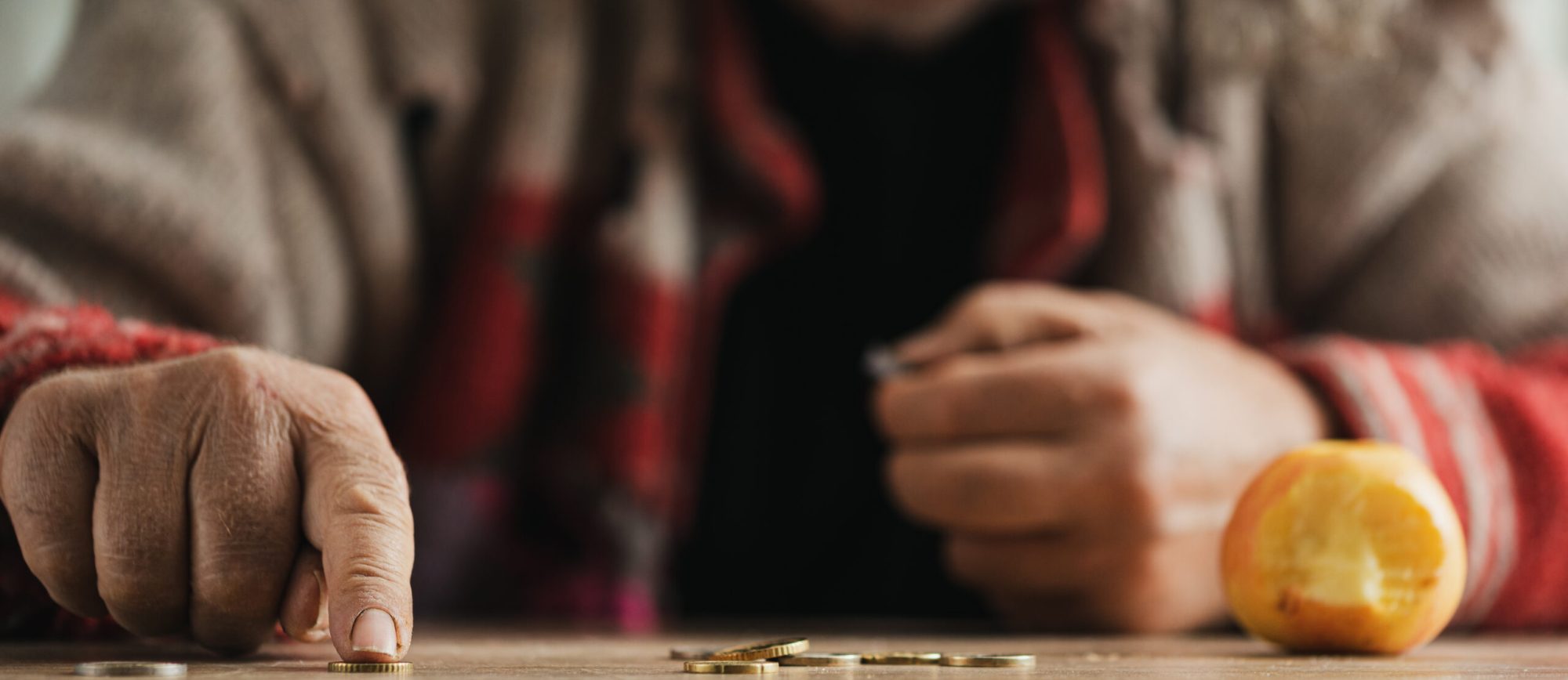 Low angle view of senior homeless man counting coins with a bitten apple on a desk.