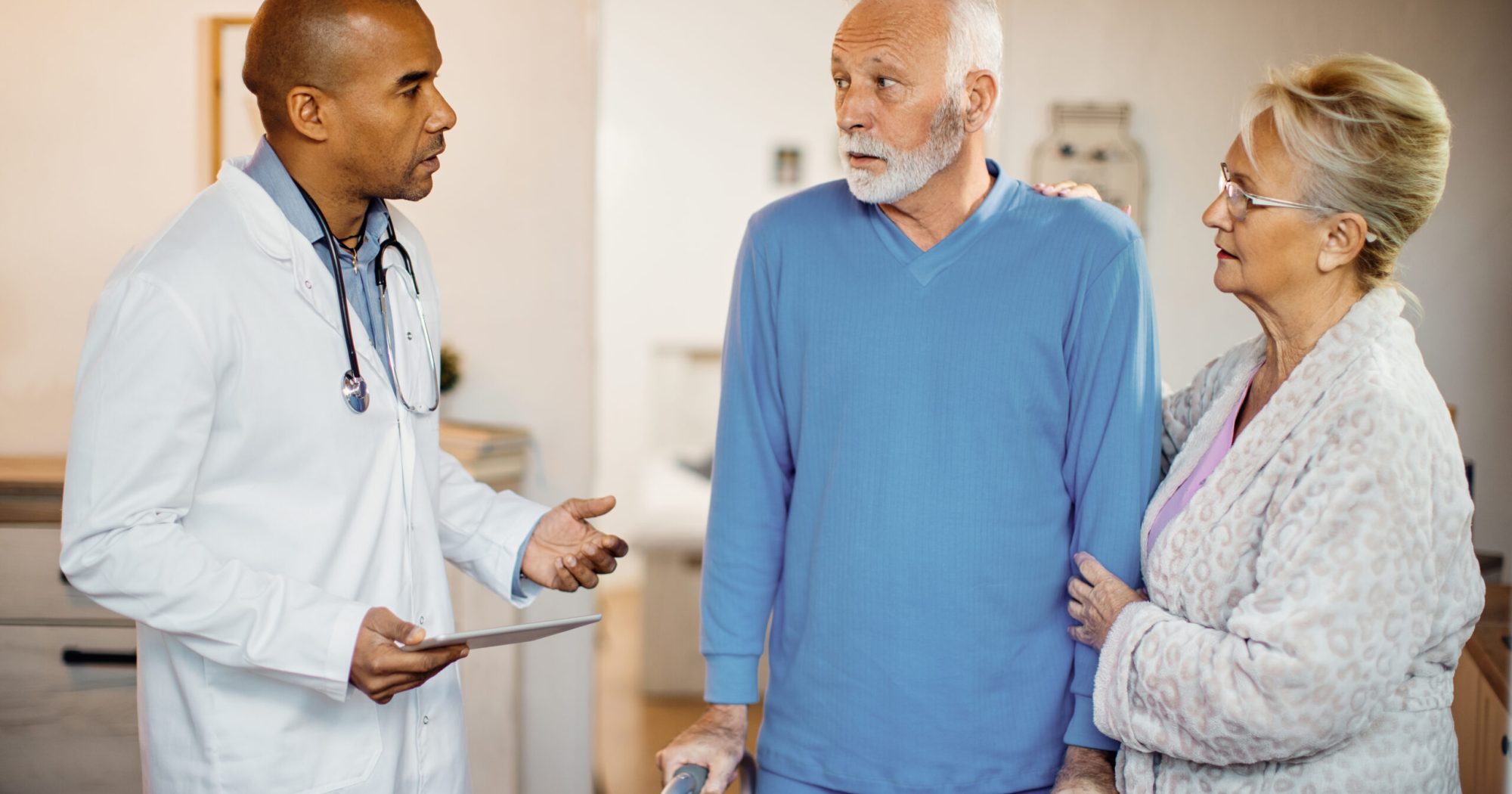 Black doctor using touchpad and communicating with senior couple while visiting them at nursing home.
