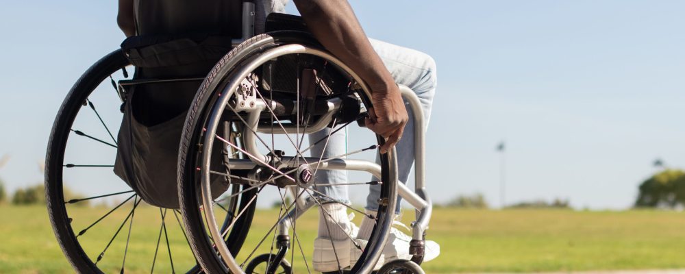Black man in wheelchair riding along park road. African American guy with disability enjoying warm summer day outside. Closeup shot of wheels. Back view. Disability, lifestyle concept.