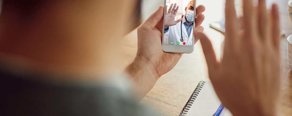 Close-up of a man waving to his doctor during video call over smart phone. Focus is on touchscreen.