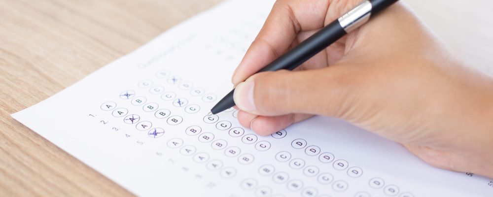 Closeup of hand holding pen and filling out questionary form on table