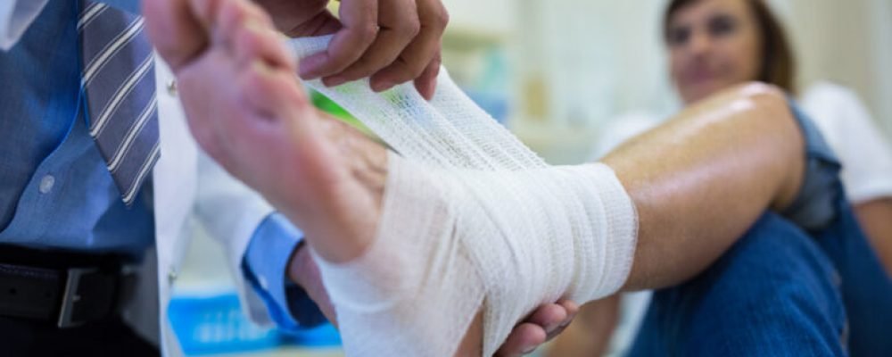 Male doctor bandaging foot of female patient in hospital