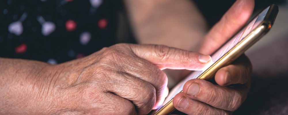Hands of an elderly woman holding a mobile phone, close up.