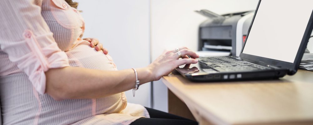 midsection-view-pregnant-woman-using-laptop-wooden-desk