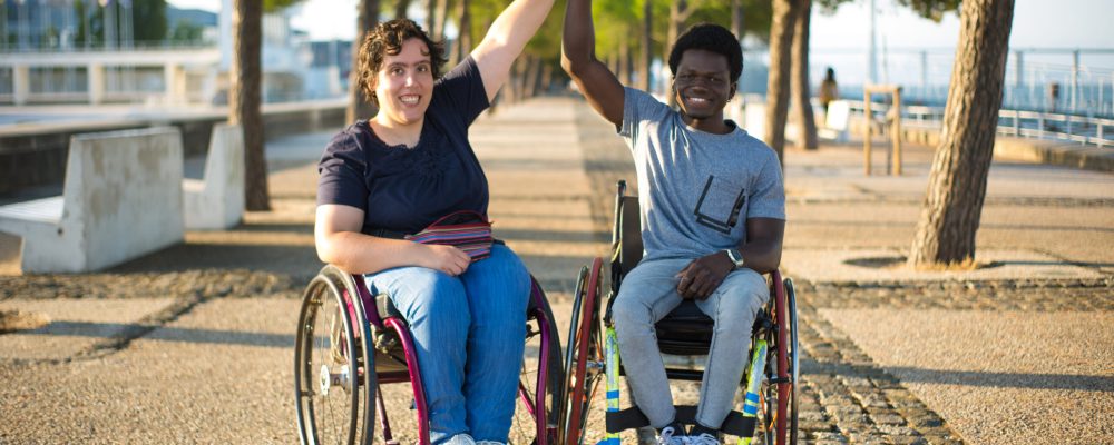 Portrait of biracial family on romantic date in park. African American man and Caucasian woman in wheelchairs, holding hands, smiling. Love, relationship, happiness concept